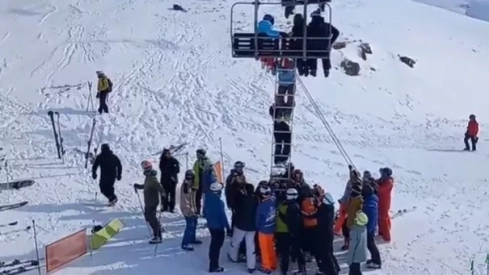 Un grupo de personas ayudan a bajarse del telesilla a unos esquiadores.